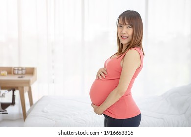 Schwangere, die sich um ihr Kind kümmert, indem sie das Kind im Schlafzimmer in ihrem trächtigen Bauch hält
