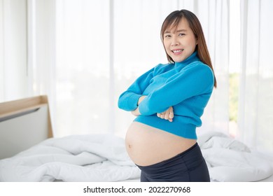Pregnant woman taking care of her child by holding baby in her pregnant belly in the bedroom	