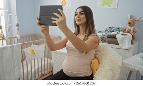 Pregnant woman taking selfie in cozy baby room with cradle, surrounded by soft toys and baby essentials, capturing a joyful indoor moment.