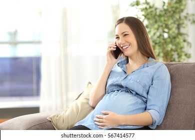 Schwangere Frau, die auf dem Handy sitzt auf einem Sofa im Wohnzimmer zu Hause