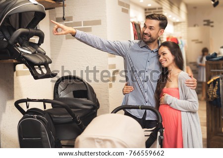 A pregnant woman together with a man choose a baby carriage. They together came for shopping in the shopping center. They are preparing to become parents and choose things for their future child.