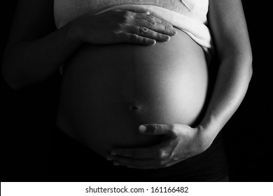Pregnant woman touching her belly with hands, close up, black and white.