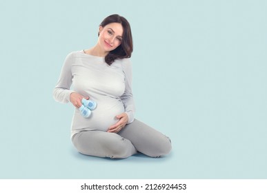 Pregnant Woman touching her belly. Pregnant middle aged mother's hands caressing her tummy. Healthy Pregnancy concept, Sitting Gravid female on blue background, full length portrait
