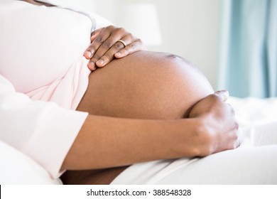 Pregnant woman touching her belly in bedroom