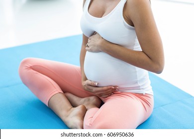 Pregnant woman touching her stomach and smiling while exercising