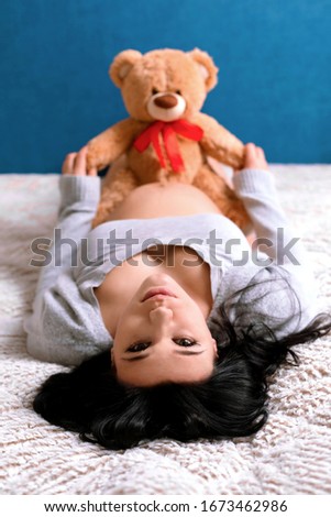 pregnant woman with toy bear on the belly, lying on the bed, happy motherhood concept