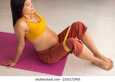 Pregnant woman training legs doing prenatal pregnancy clamshell sitting hip exercise with resistance bands preparing for birth. Asian girl doing workout seated pilates fitness exercises