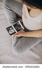 Pregnant Woman With Ultrasound Photo Sitting On Bed