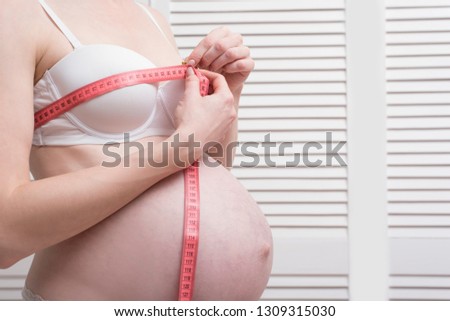 Pregnant woman in underwear is measuring her breasts with a measuring tape