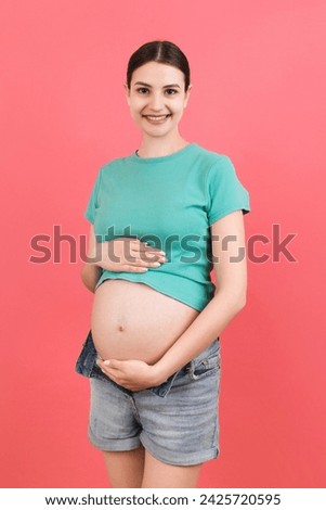 pregnant woman in unzipped jeans showing her baby bump at colorful background with copy space. Waiting for a baby concept.