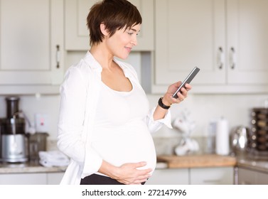 Pregnant woman using her smartphone at home in the kitchen - Powered by Shutterstock