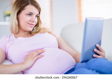 Pregnant woman using tablet at home in the living room - Powered by Shutterstock