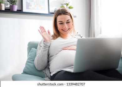 Pregnant Woman Video Chatting With Family On Laptop Waving Hand To Screen