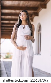 A pregnant woman is walking down the street. Happy girl in a white dress