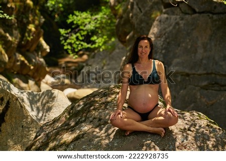a  pregnant woman wearing a bikini relaxes in a mountain river