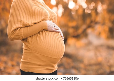 Pregnant woman wearing knitted yellow sweater holding belly outdoors. Maternity. Motherhood. 20s. 