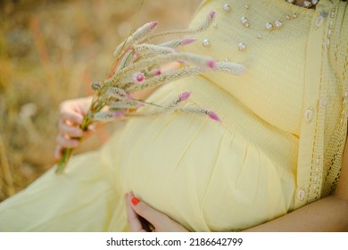 Pregnant woman, wearing light yellow dress, holding in hands  bouquet of daisy flowers ."selective focus" "shallow depth of field" "follow focus" or " blur".