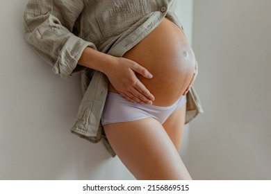 Pregnant woman wearing maternity underwear pajamas at home relaxing holding expecting tummy for skincare, health, lifestyle. Pregnancy belly closeup for cellulite and stretch marks