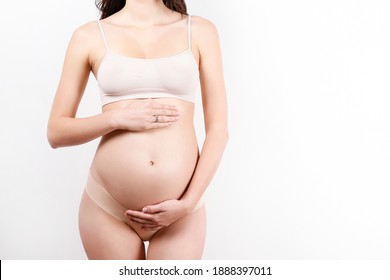 Pregnant woman wearing supportive seamless maternity bra and body color bottoms, arms on her belly. Female hands wrapped around bare tummy. Pregnancy underwear concept. Background, copy space.