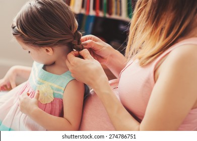 pregnant woman weaving braids with her toddler daughter at home - Powered by Shutterstock