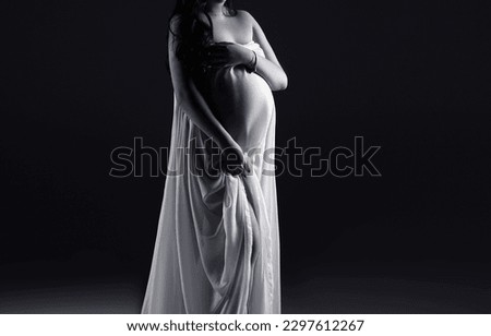 Pregnant woman in a white dress on a black background. Copy space. Pregnancy.
