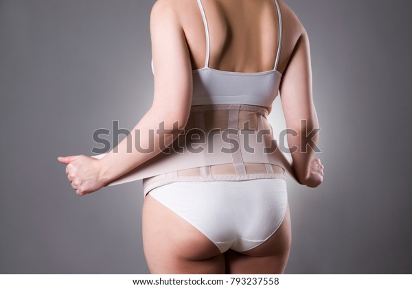 Pregnant woman in\
white underwear with orthopedic support belt, pregnancy bandage,\
studio shot on gray\
background