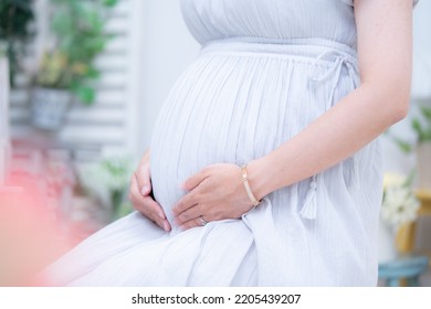 A Pregnant Woman Who Puts Her Hand On Her Stomach With A Maternity Dress Indoors (shooting A Real Pregnant Woman)