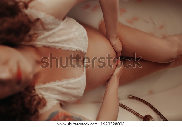 a pregnant woman without a face lies in a milk bath\
of white water in a delicate bra made of transparent fabric and\
strokes her large tummy