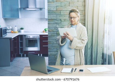 pregnant woman working as freelancer at home with laptop and tablet - Powered by Shutterstock