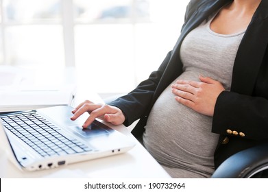 Pregnant woman working on laptop. Cropped image of pregnant businesswoman typing something on laptop while sitting at her working place in office  - Powered by Shutterstock