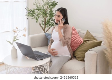 Pregnant woman working on laptop and smart phone in the living room at home - Powered by Shutterstock