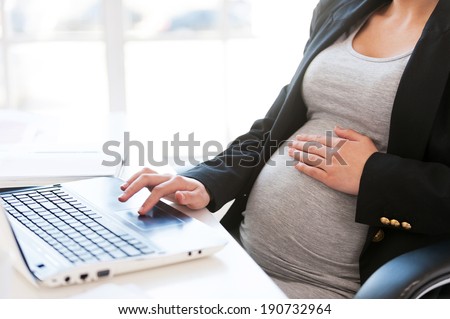 Pregnant woman working on laptop. Cropped image of pregnant businesswoman typing something on laptop while sitting at her working place in office 