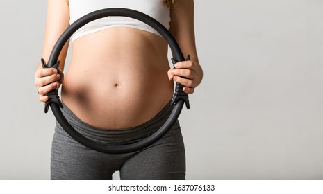 Pregnant woman in yoga pants exercising with a Pilates ring