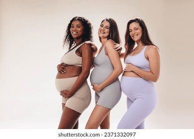 Pregnant women enjoying a diverse prenatal yoga class, bonding over their shared journey into motherhood. Friends standing in a studio with fitness clothing, happy smiles, and visible baby bumps. - Powered by Shutterstock