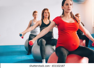 Pregnant women in a row sitting on Pilates ball and exercising with weights feeling strong