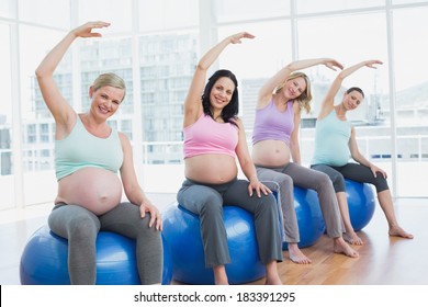 Pregnant women sitting on exercise balls stretching arms in a fitness studio