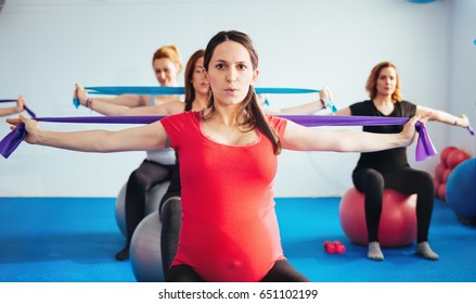 Pregnant women sitting on Pilates ball exercising and stretching workout bands 