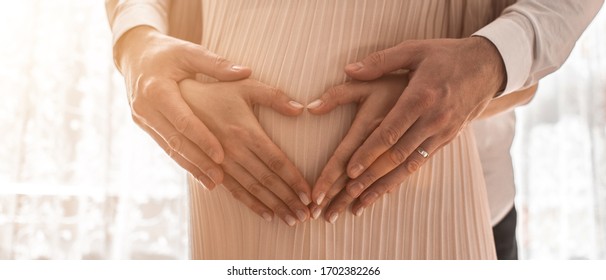 Pregnant Women Wrap Her Arms Around The Belly In The Form Of The Heart. Family Concept.