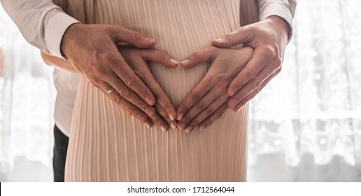 Pregnant Women Wrap Her Arms Around The Belly In The Form Of The Heart. Family Concept.