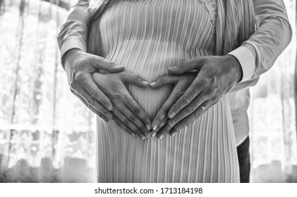 Pregnant Women Wrap Her Arms Around The Belly In The Form Of The Heart. Family Concept.