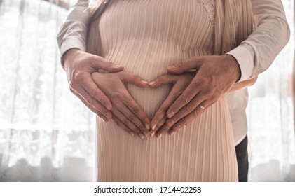 Pregnant Women Wrap Her Arms Around The Belly In The Form Of The Heart. Family Concept.