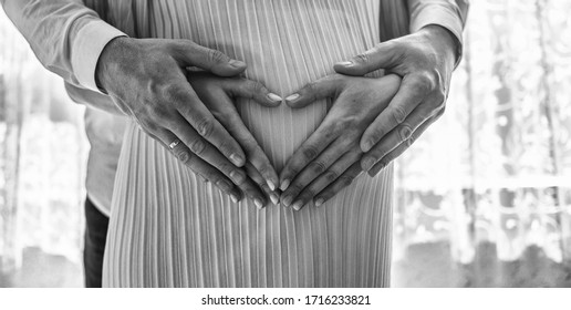 Pregnant Women Wrap Her Arms Around The Belly In The Form Of The Heart. Family Concept.