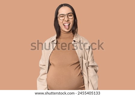 Pregnant young Caucasian woman showcasing maternity on studio background funny and friendly sticking out tongue.