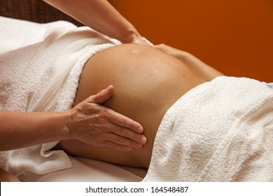 Pregnant Young Latina Woman With Beautiful Skin, Being Wrapped With A Towel, Lying On A Bed And Having A Relaxing Prenatal Massage, Various Techniques