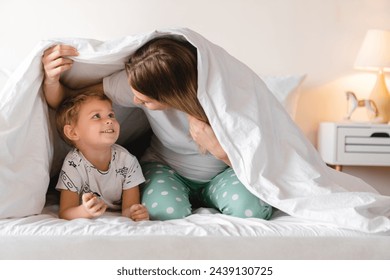 Pregnant young mother playing with her toddler little son hiding under the blanket on a bed together. Family moments, children care. Motherhood, maternity leave concept - Powered by Shutterstock