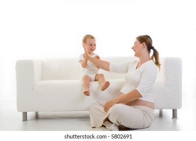 Pregnant Young Woman Playing With A Toddler Sitting On A White Couch...isolated View With Mostly White Tones.