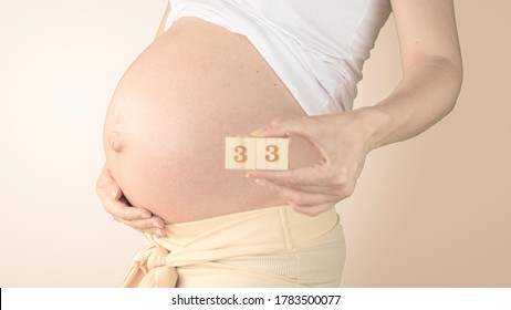 Pregnant young woman with pregnancy week number next to her belly. Photos of belly growth at 33 weeks pregnancy. Healthy pregnancy diet and fetal development.