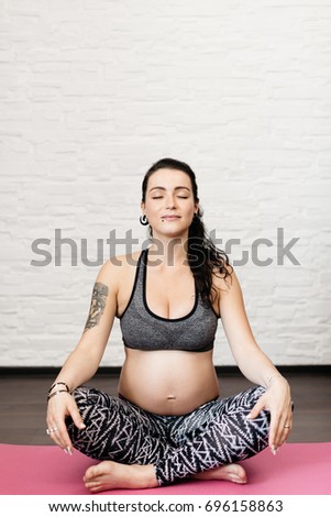 Pregnant young woman relaxing and sitting cross legged on a fitness mat