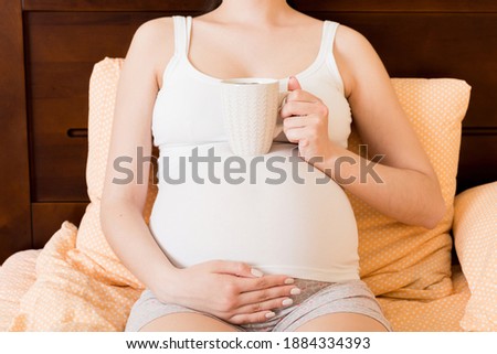 pregnant young woman sitting on bed and drinking coffee at home. maternity concept.