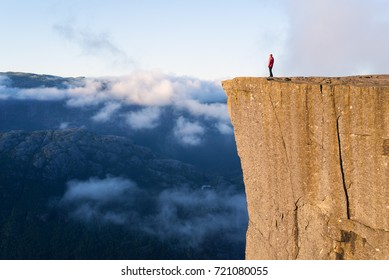 Preikestolen - amazing rock in Norway. Girl standing on a cliff above the clouds. Pulpit Rock, the most famous tourist attraction in Ryfylke, towers over the Lysefjord - Shutterstock ID 721080055